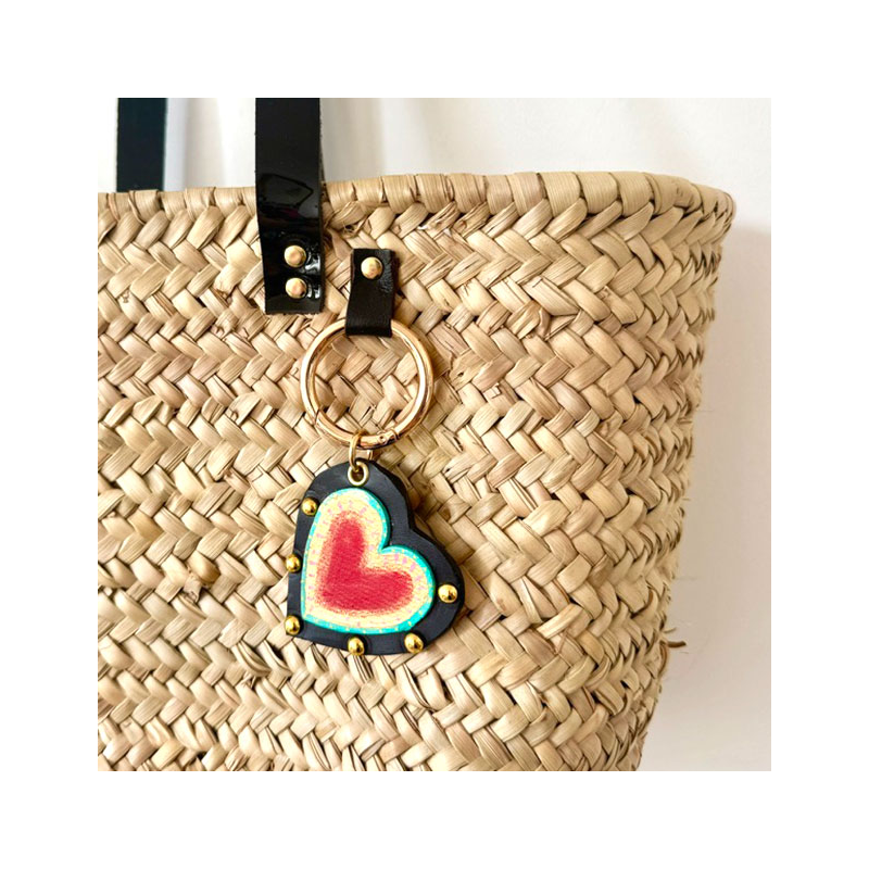 Bijou de panier cœur sacré en cuir noir et rouge accroché sur un panier en paille artisanale